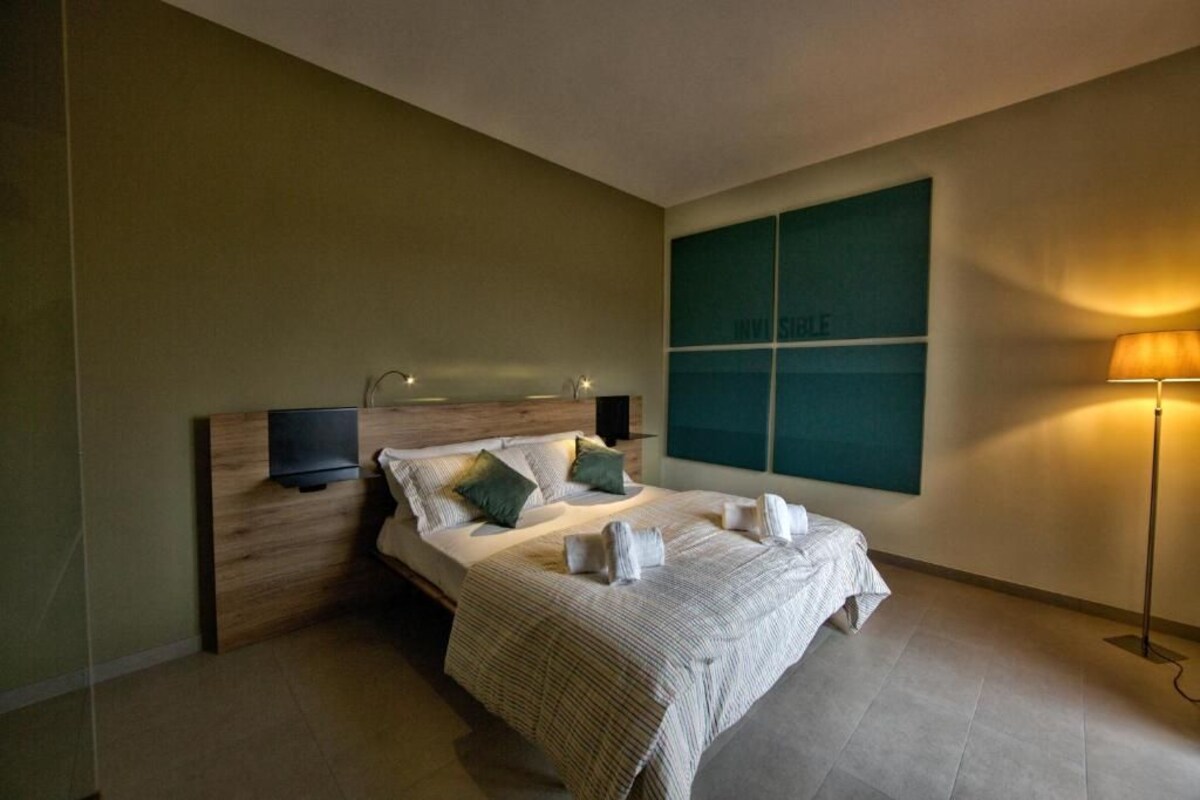 A modern hotel room with a large bed, a flat-screen TV, a bedside table, and a wall-mounted artwork.