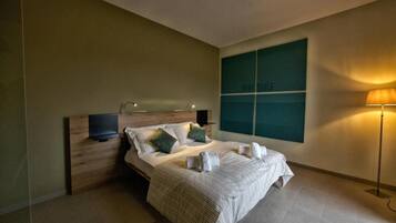 A modern hotel room with a large bed, a flat-screen TV, a bedside table, and a wall-mounted artwork.