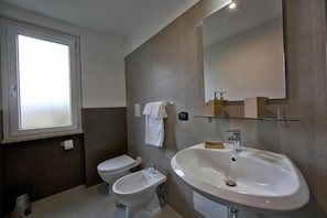 A modern bathroom with a toilet, bidet, and a large sink with a mirror above.