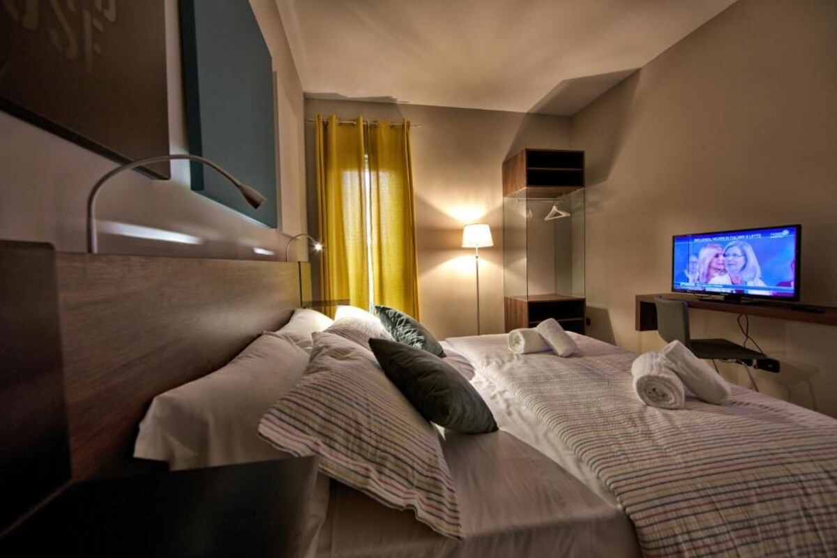 A hotel room with two beds, a television, a mirror, and a window with curtains.