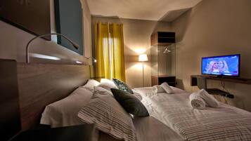 Een hotelkamer met twee bedden, een televisie, een spiegel en een raam met gordijnen.