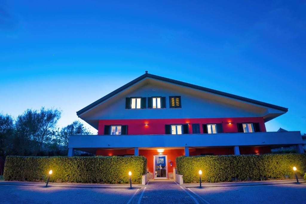 Un hotel moderno con fachada roja y blanca, una entrada central y un camino de acceso bien iluminado.