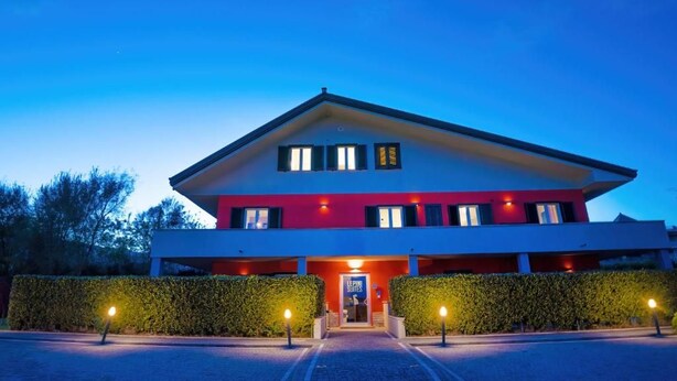 A modern hotel with a red and white facade, a central entrance, and a well-lit driveway. - Lepini Suites Guesthouse (Patrica)