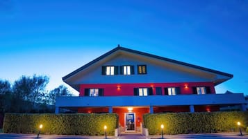 Un hotel moderno con fachada roja y blanca, una entrada central y un camino de acceso bien iluminado.