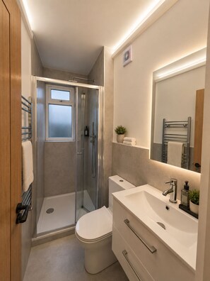 Ein modernes Badezimmer mit einer Duschkabine, einer weißen Toilette, einem Waschtisch mit Spiegel und einem Handtuchhalter.