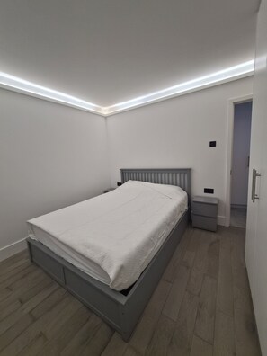 Ein Schlafzimmer mit einem Bett, Nachttischen und einer Tür zu einem anderen Raum.