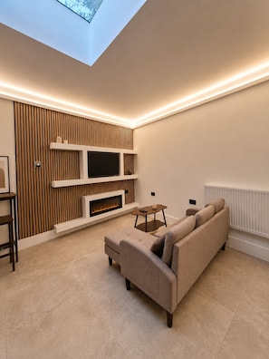 A modern living room with a flat-screen TV, a fireplace, and a sofa. - Modern Skylight Home (London)