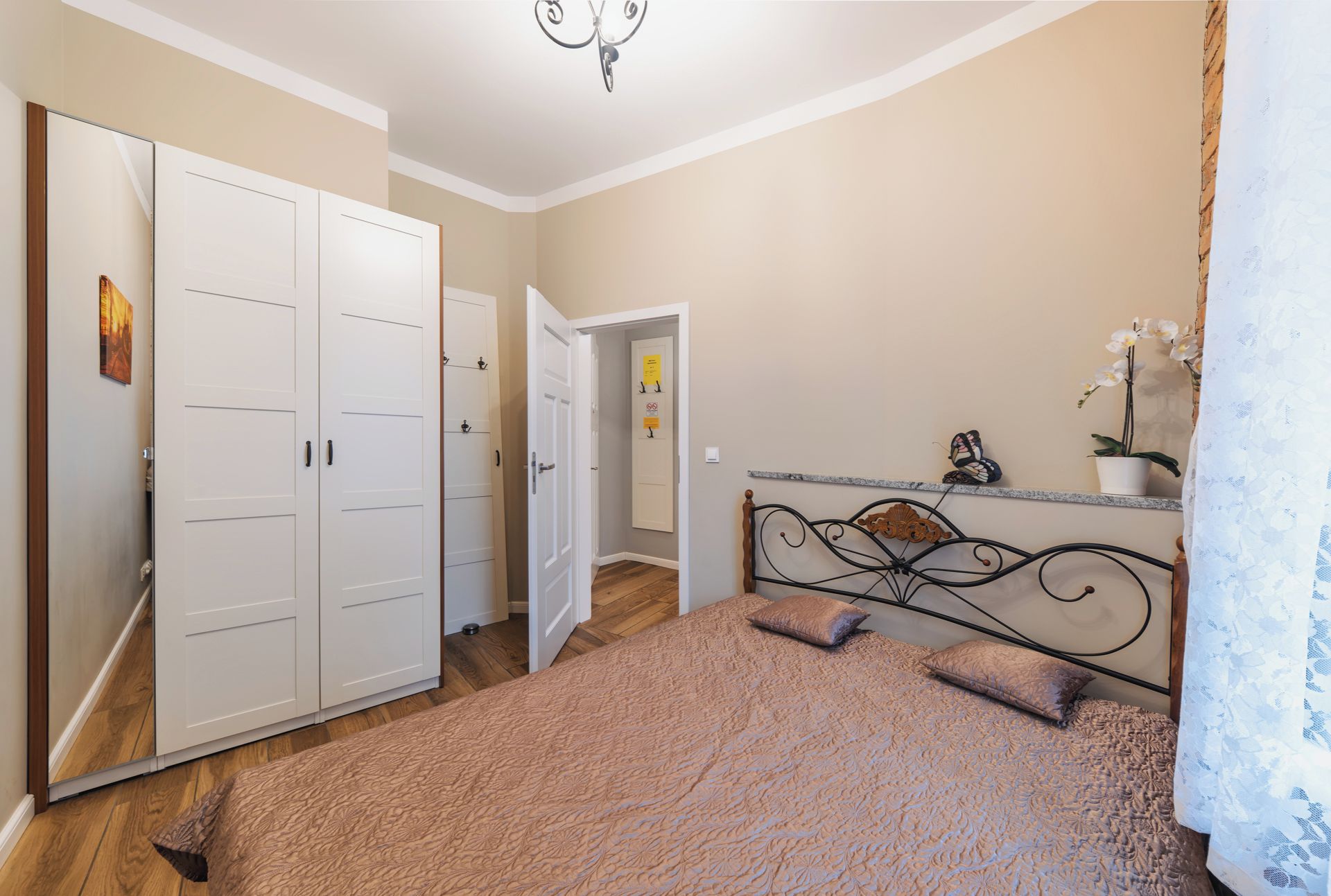Un dormitorio con una cama, un armario, una puerta y un pequeño estante con una planta.