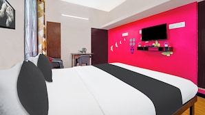 Ett hotellrum med en säng, ett skrivbord med en stol, en tv och en vägg som är accentuerad med rött.
