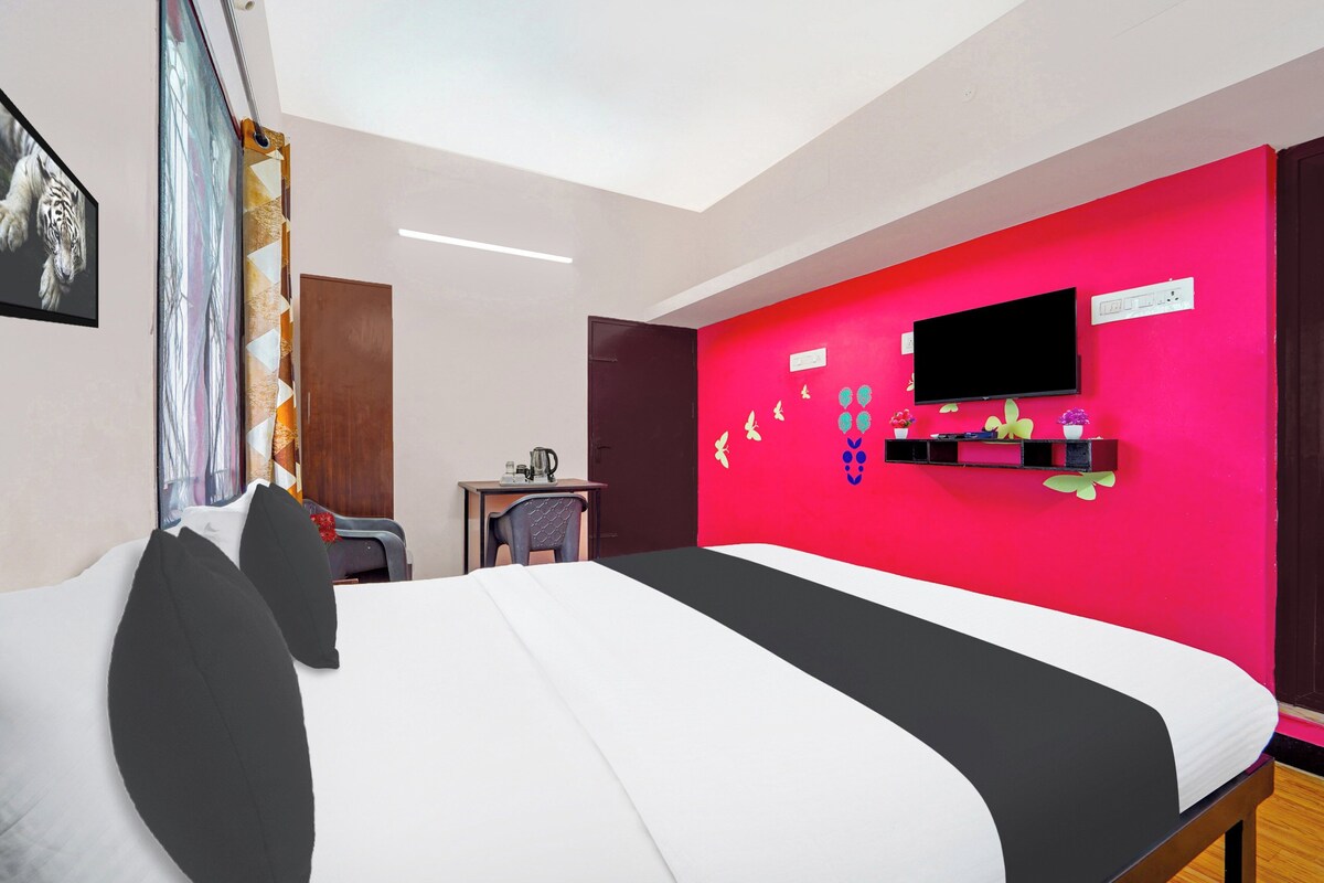 Una habitación de hotel con una cama, un escritorio con una silla, un televisor y una pared de acento roja.