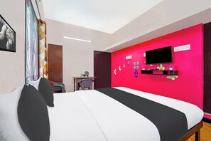 Una habitación de hotel con una cama, un escritorio con una silla, un televisor y una pared de acento roja.