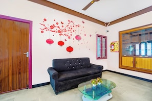 Una sala de estar con un sofá oscuro, una mesa de centro de vidrio con flores y una pared decorada con detalles rojos.