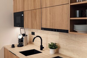 A modern kitchen with wooden cabinets, a built-in microwave, a coffee machine, a sink, and a small potted plant. - R18 Residences Prague (Hlavní město Praha)