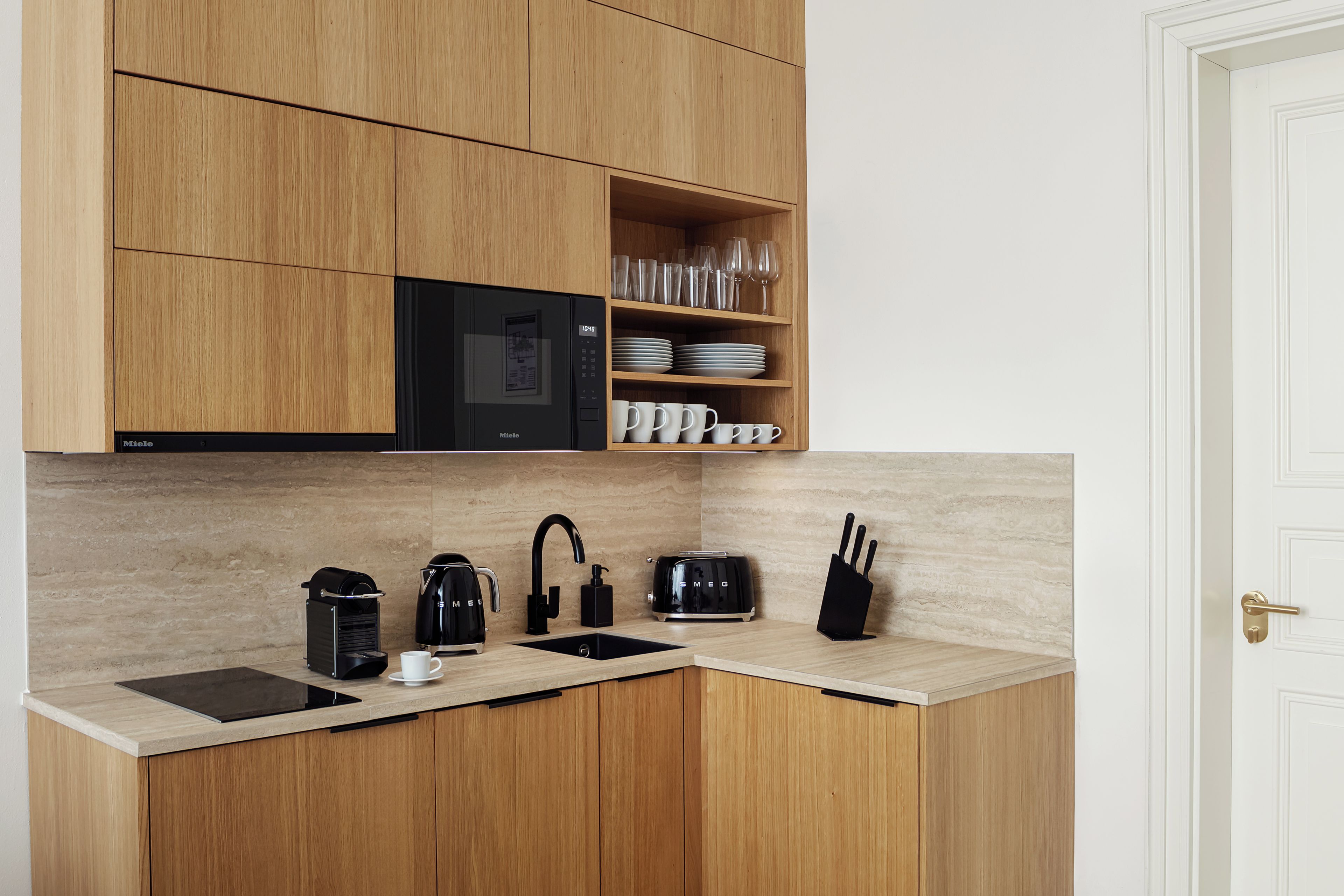 A modern kitchen with wooden cabinets, a black microwave, a coffee machine, a toaster, and a knife block.