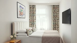 A neatly arranged bedroom with a bed, pillows, a bedside table with books, and a wall-mounted TV. - R18 Residences Prague (Hlavní město Praha)