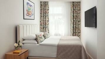 A neatly arranged bedroom with a bed, pillows, a bedside table with books, and a wall-mounted TV.