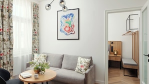 A modern living room with a grey sofa, a round wooden table, and a potted plant. - R18 Residences Prague (Hlavní město Praha)