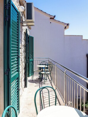 A balcony with a table and chairs, a hose, and a building with a white wall and green shutters. - Stone house in the very center with pool table, two balconies and the sea view (Bol)