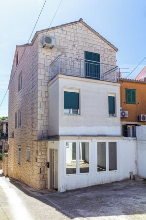 A two-story building with a balcony on the upper floor, a visible entrance, and a small outdoor area. - Stone house in the very center with pool table, two balconies and the sea view (Bol)