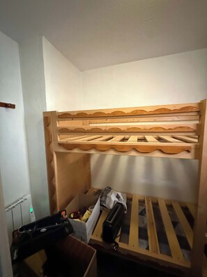 A bunk bed with a wooden frame and slatted headboard, a small storage box, and a black object on the lower bunk. - "V24" by Versant Collection (Les Belleville)