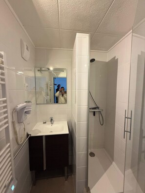 A bathroom with a glass-enclosed shower, a sink with a mirror, and a hairdryer on the wall. - "V24" by Versant Collection (Les Belleville)