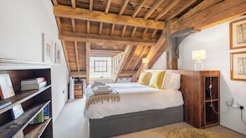 A bedroom with a wooden ceiling, a bed with pillows, a bedside table with a lamp, and a bookshelf.