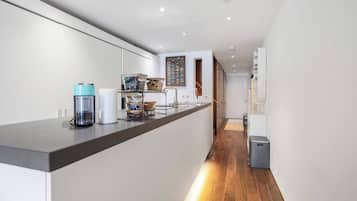 A modern kitchen with a long countertop, a coffee machine, and a trash bin.