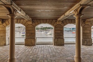 A covered area with stone columns and arches, overlooking a marina with boats. - Luxury 2bed Apartment in historic RoyalWilliamYard (Plymouth)