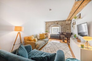 A living room with a sofa, a lamp, a piano, and a television. - Luxury 2bed Apartment in historic RoyalWilliamYard (Plymouth)