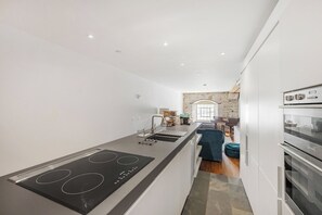 A modern kitchen with a central island, built-in oven, and a stone accent wall. - Luxury 2bed Apartment in historic RoyalWilliamYard (Plymouth)