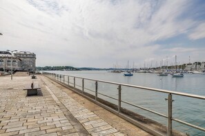 A waterfront promenade with a stone walkway, metal railing, and a row of boats. - Luxury 2bed Apartment in historic RoyalWilliamYard (Plymouth)