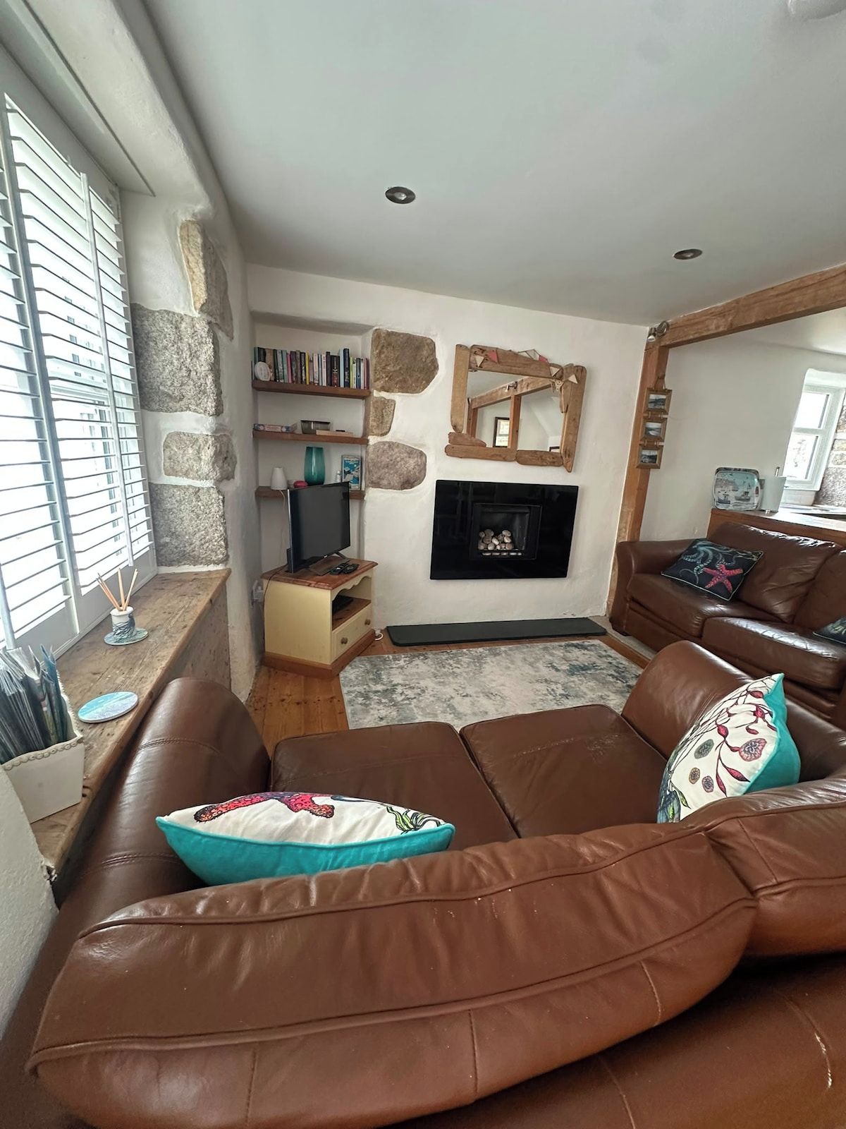 A living room with a brown leather sofa, a fireplace, a stone wall, and a bookshelf.