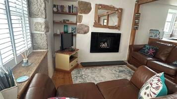 A living room with a brown leather sofa, a fireplace, a stone wall, and a bookshelf.