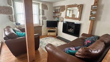 A living room with a brown leather sofa, a television, a fireplace, and stone wall accents.