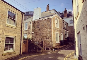 Una calle estrecha con edificios de piedra, una escalera visible y cielo despejado.