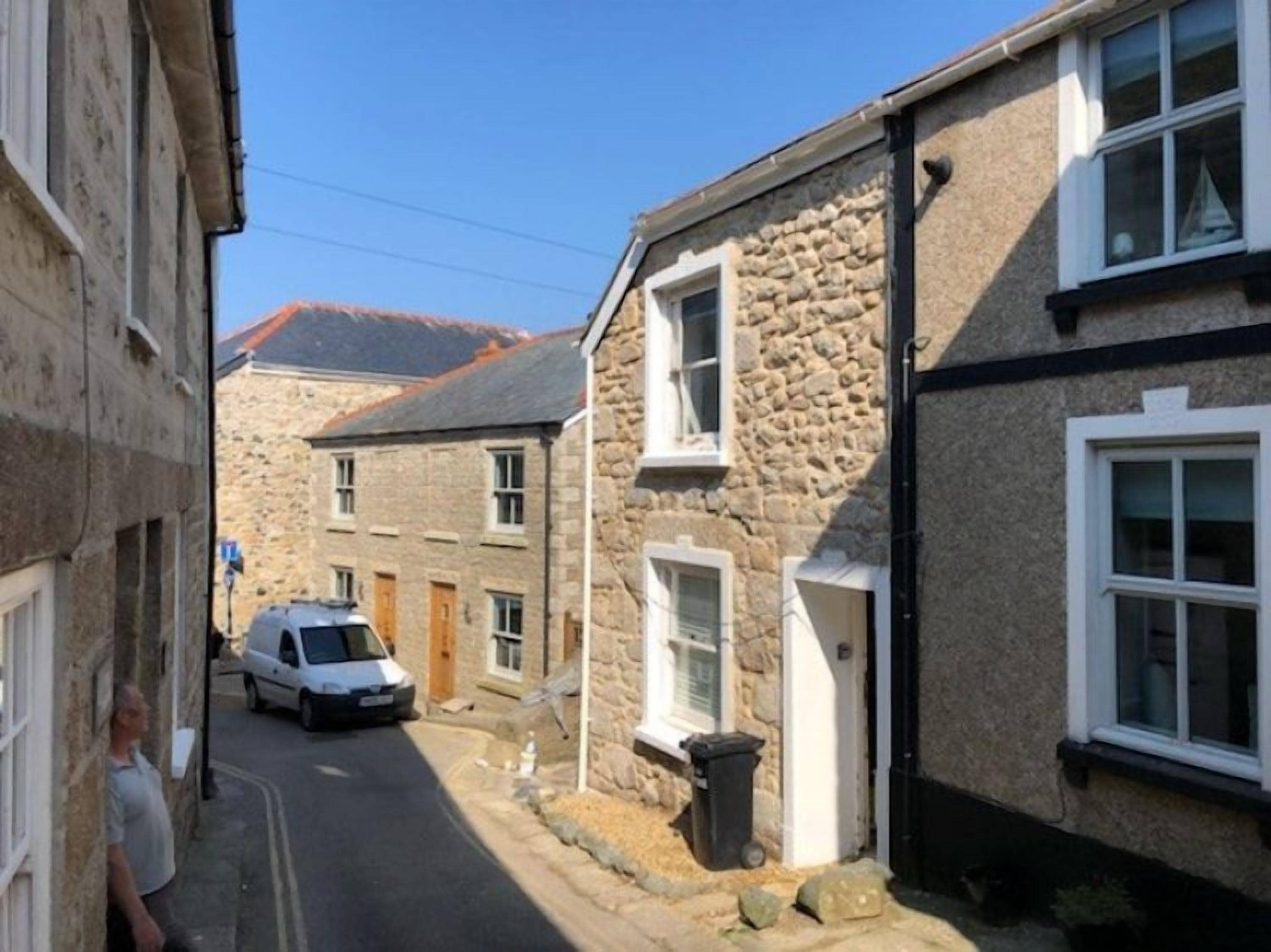 A narrow street with stone buildings, a parked car, and a clear sky.