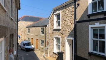 A narrow street with stone buildings, a parked car, and a clear sky.