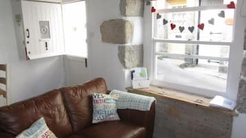 Una stanza con un divano in pelle marrone, una finestra decorata con cuori, un muro in pietra e un tavolino con un libro.