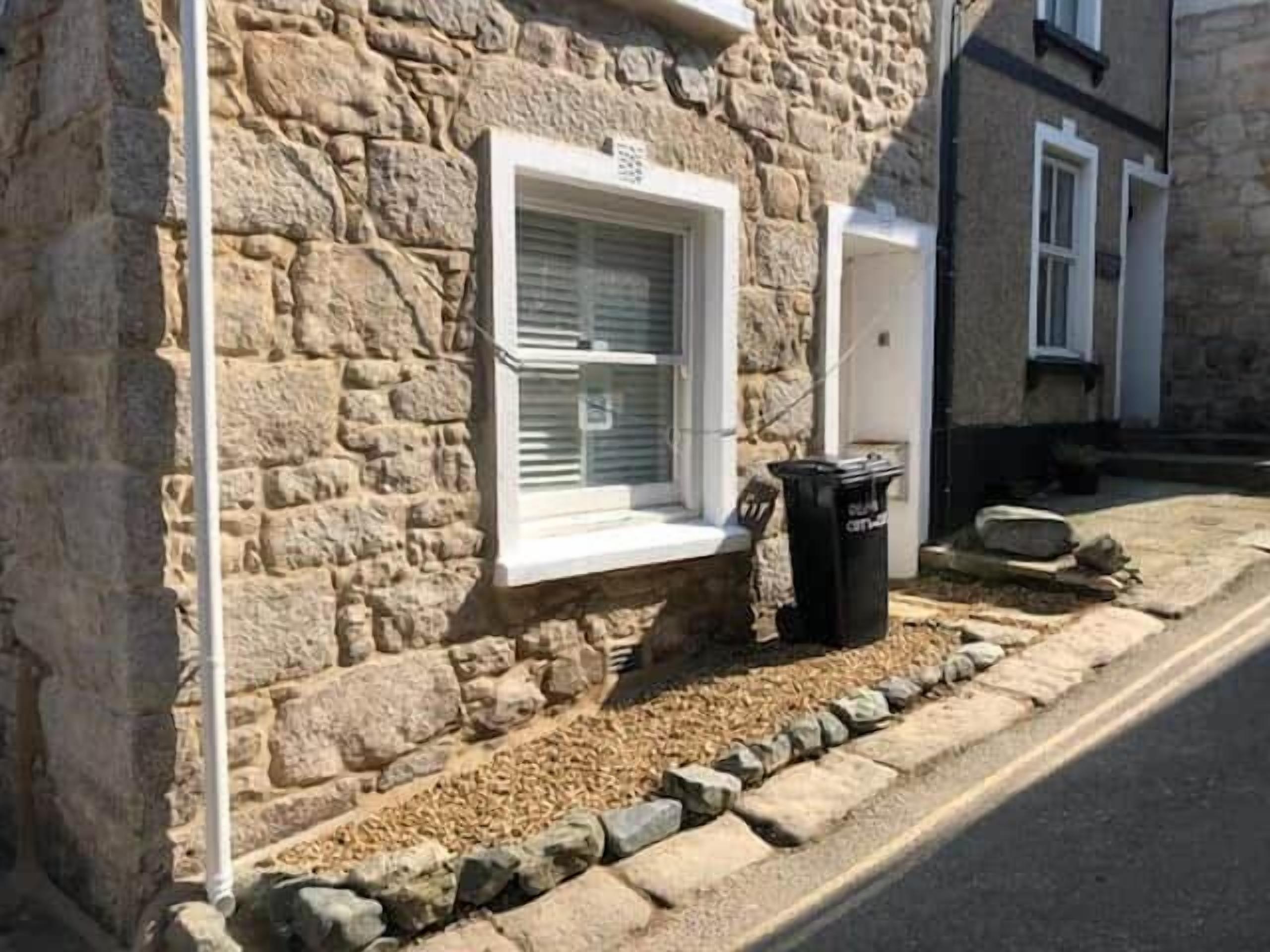 A stone building with a window and a trash bin.