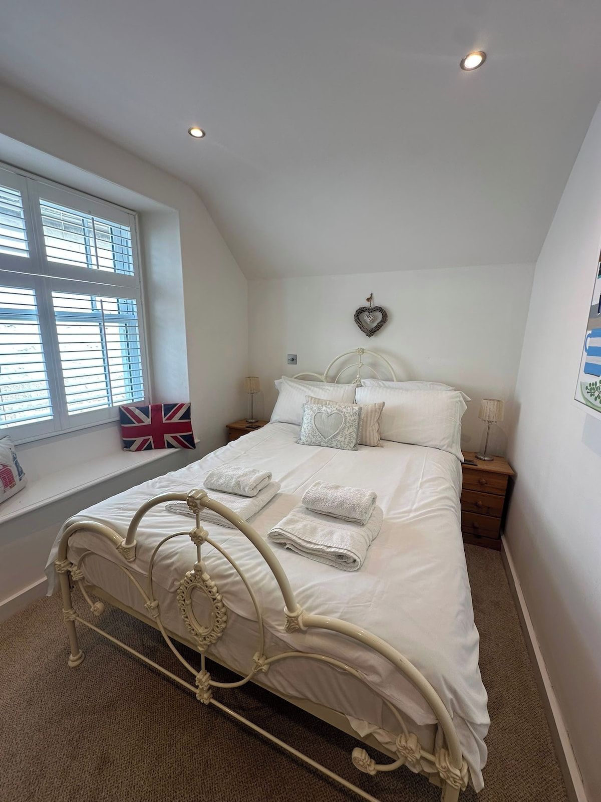 A bedroom with a bed, bedside tables, a window with blinds, and a wall decoration.