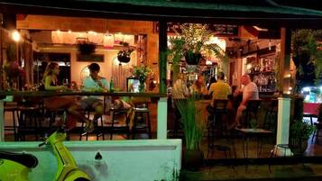 An outdoor seating area with tables and chairs, a bar area with stools, and a scooter parked in the foreground.
