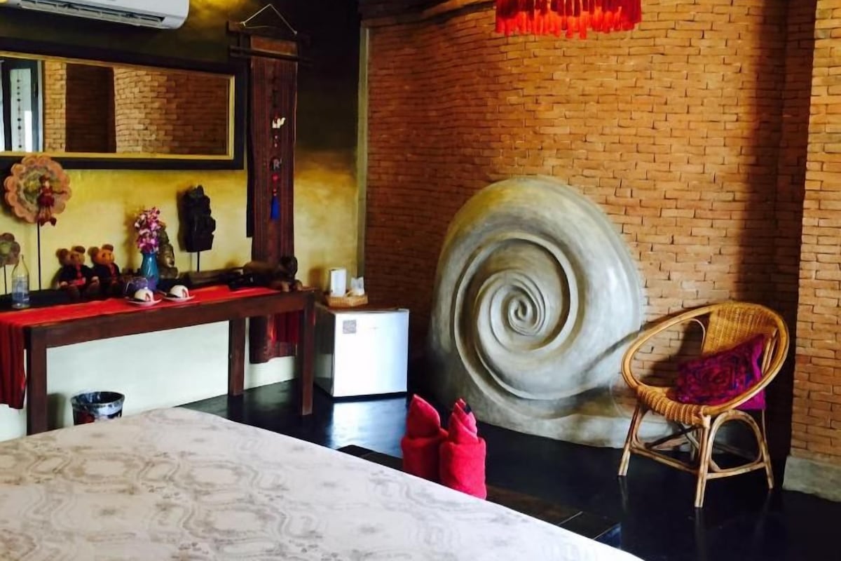 A room with a large bed, a round decorative wall piece, a wicker chair, and a hanging light fixture.