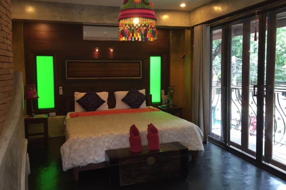 Un dormitorio con una cama grande, una lámpara colgante decorativa y vistas a través de un ventanal.