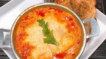 Eine Schüssel Suppe mit Garnitur auf einem weißen Teller, dazu eine Brotscheibe und ein kleiner Salat auf einem Holztisch.