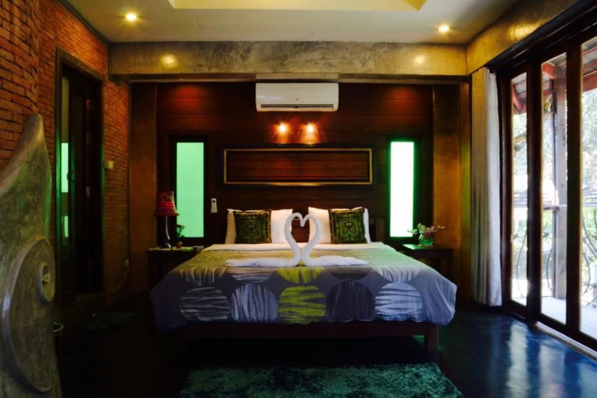 A hotel room with a bed, a headboard, an air conditioning unit, and a view through the window.