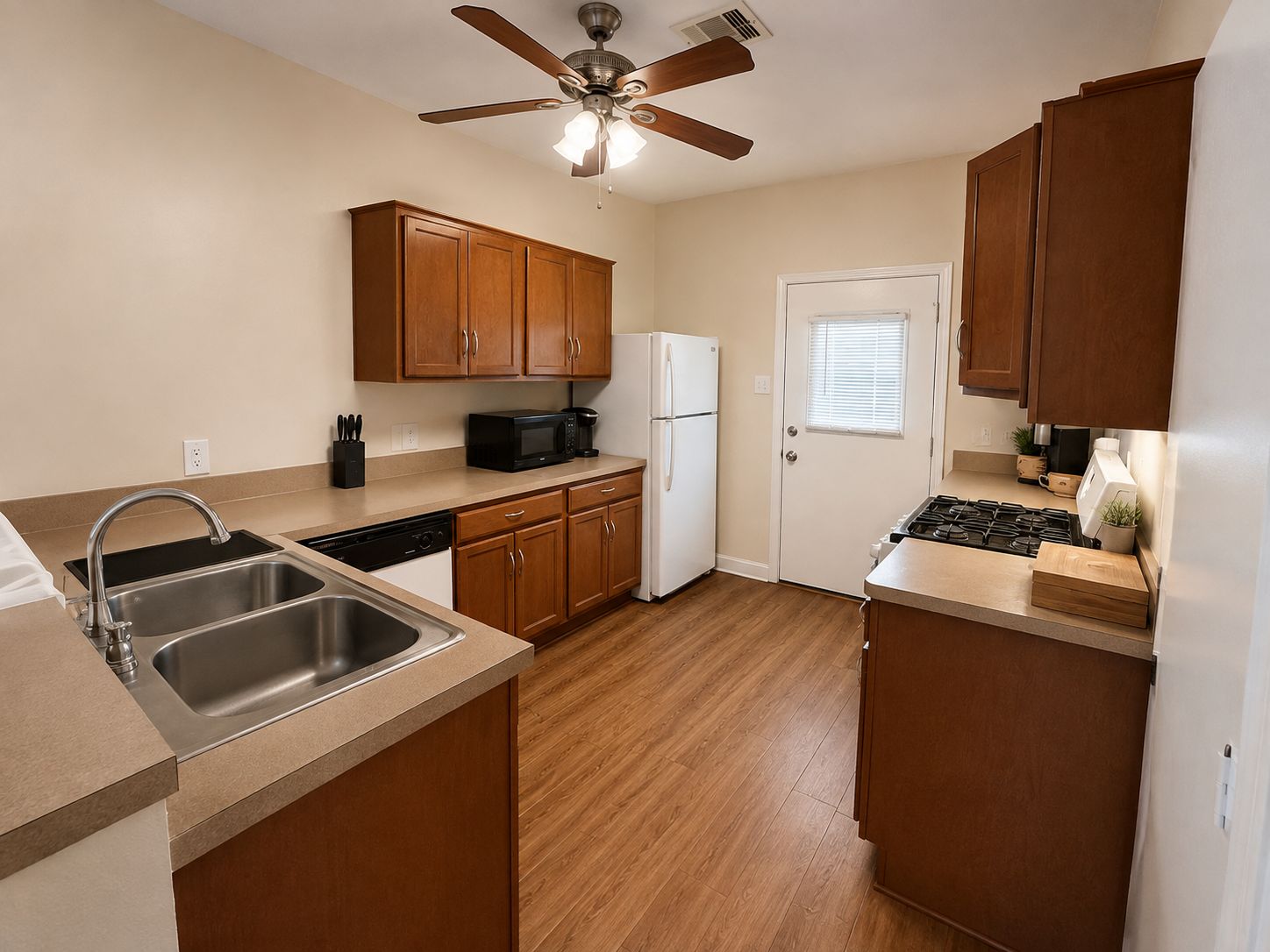 A kitchen with wooden cabinets, a dishwasher, a microwave, a refrigerator, a stove, and a ceiling fan.