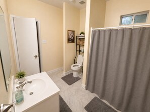 Ein Badezimmer mit einem weißen Waschbecken, einer Toilette, einer Duschvorhang und einem kleinen Regal mit einer Pflanze.