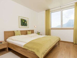 A bedroom with a wooden bed, a nightstand, a bedside table, a window with curtains, and a wall-mounted picture. - "green" on the Sandwiesen Farm (Gargazzone)