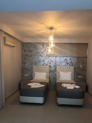 Een hotelkamer met twee bedden, een wand met marmerlook, een moderne hanglamp en een airconditioning.