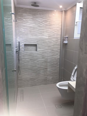 Een moderne badkamer met een douche met glazen wand, een toilet en een wastafelmeubel.